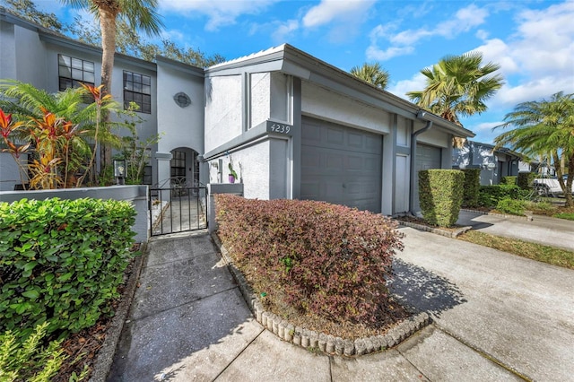 view of front facade with a gate, stucco siding, an attached garage, and concrete driveway