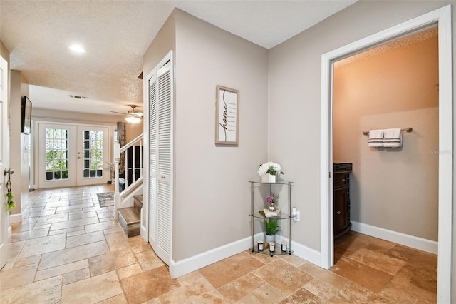 hallway with a textured ceiling, baseboards, french doors, stairway, and stone tile flooring