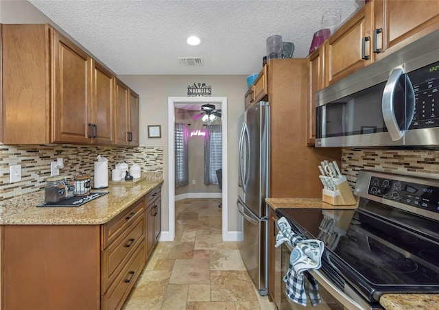 kitchen featuring appliances with stainless steel finishes, stone tile flooring, visible vents, and brown cabinets