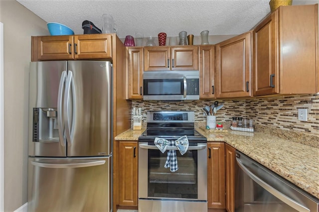 kitchen featuring brown cabinetry, light stone counters, stainless steel appliances, and backsplash