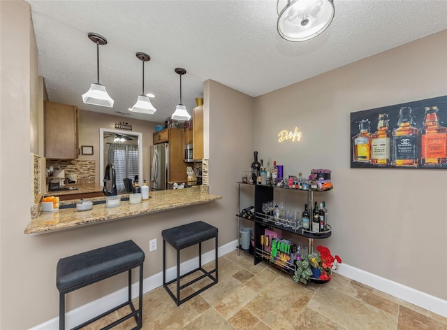 kitchen featuring baseboards, brown cabinetry, decorative backsplash, appliances with stainless steel finishes, and a peninsula