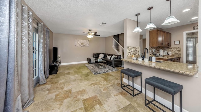 kitchen with a breakfast bar, tasteful backsplash, brown cabinetry, a sink, and baseboards