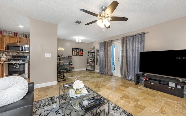 living area featuring ceiling fan, a textured ceiling, visible vents, baseboards, and stone tile flooring