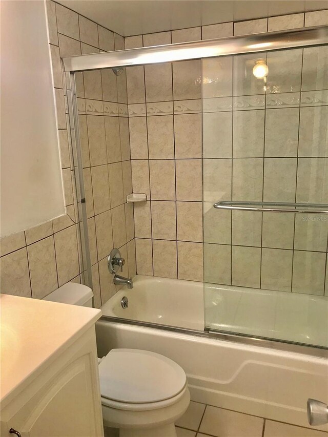 full bathroom featuring vanity, shower / bath combination with glass door, tile patterned flooring, toilet, and tile walls