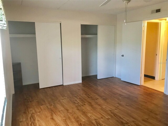 unfurnished bedroom with multiple closets, ceiling fan, and wood-type flooring