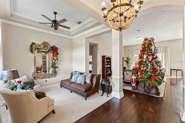 living room featuring hardwood / wood-style flooring, ceiling fan with notable chandelier, a raised ceiling, and ornamental molding