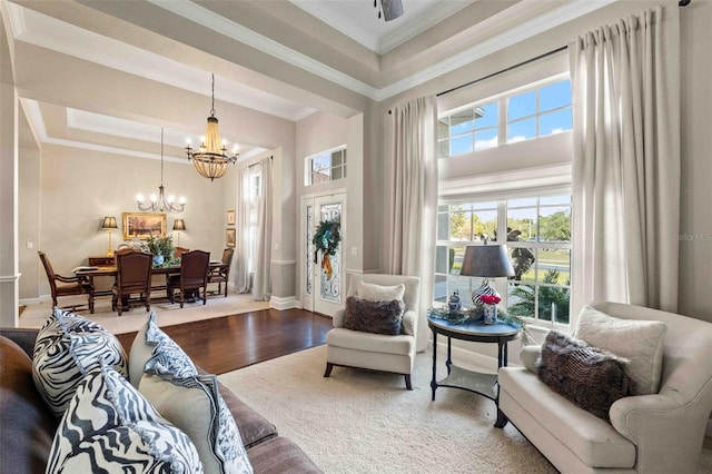 living area featuring hardwood / wood-style floors, a towering ceiling, crown molding, and a notable chandelier