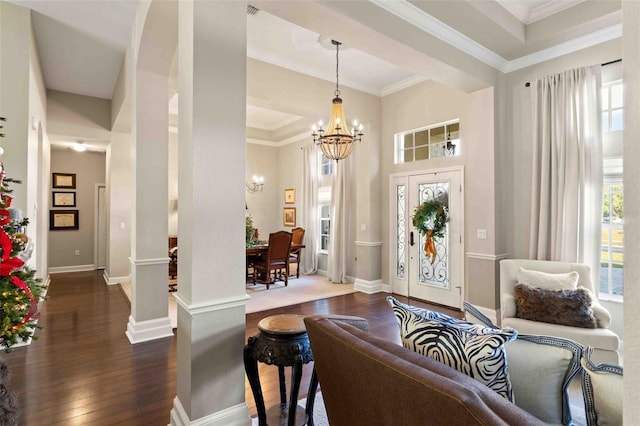 foyer entrance featuring a notable chandelier, dark hardwood / wood-style floors, ornamental molding, and decorative columns