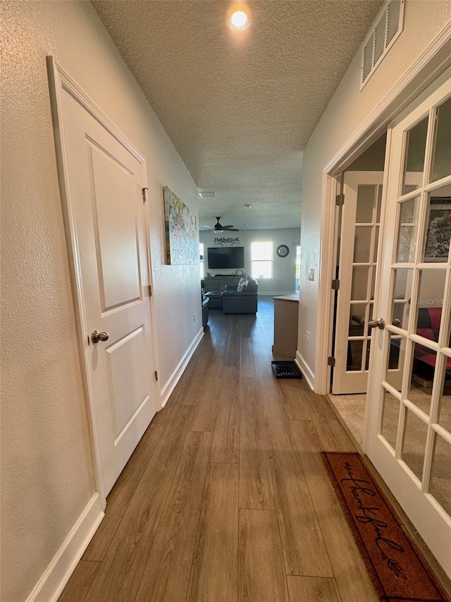 hallway with french doors, a textured ceiling, and hardwood / wood-style flooring