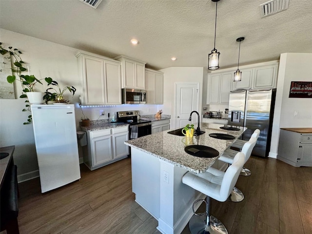 kitchen with a breakfast bar, a center island with sink, sink, light stone countertops, and stainless steel appliances