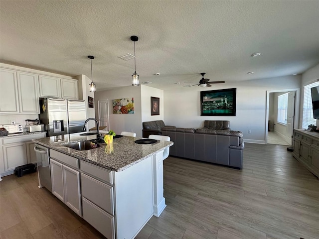 kitchen with white cabinets, an island with sink, decorative light fixtures, light stone counters, and stainless steel appliances