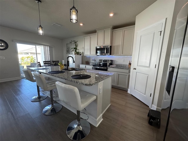 kitchen featuring pendant lighting, a center island with sink, sink, light stone countertops, and appliances with stainless steel finishes