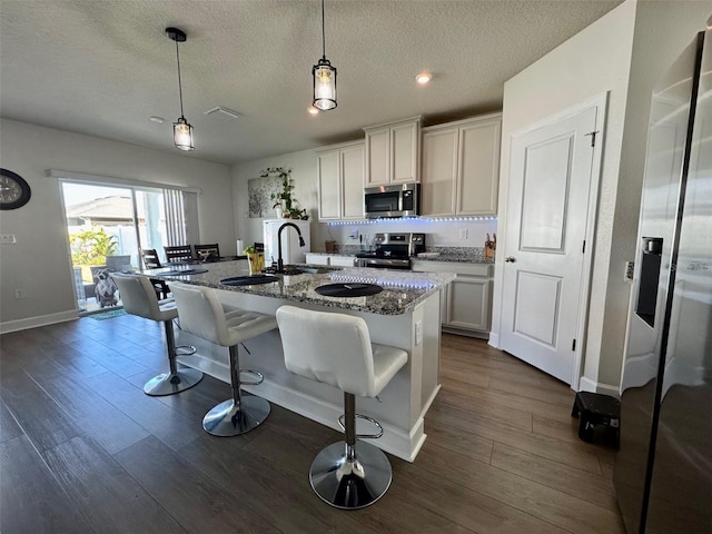 kitchen featuring dark stone counters, a textured ceiling, an island with sink, appliances with stainless steel finishes, and white cabinetry