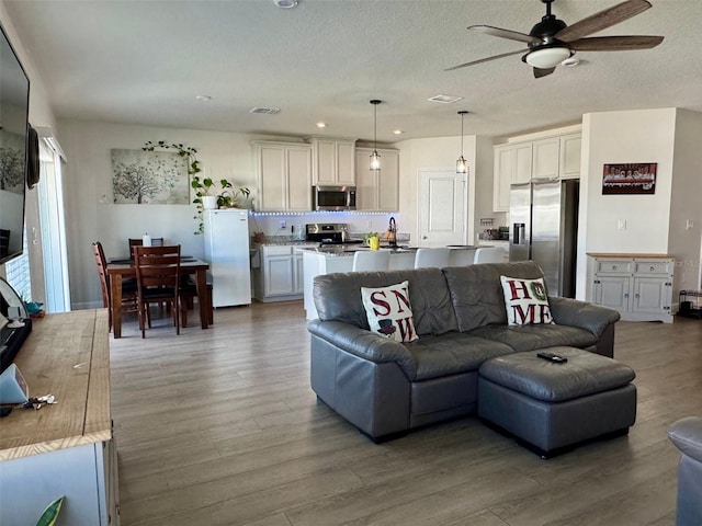 living room with hardwood / wood-style floors, a textured ceiling, and ceiling fan