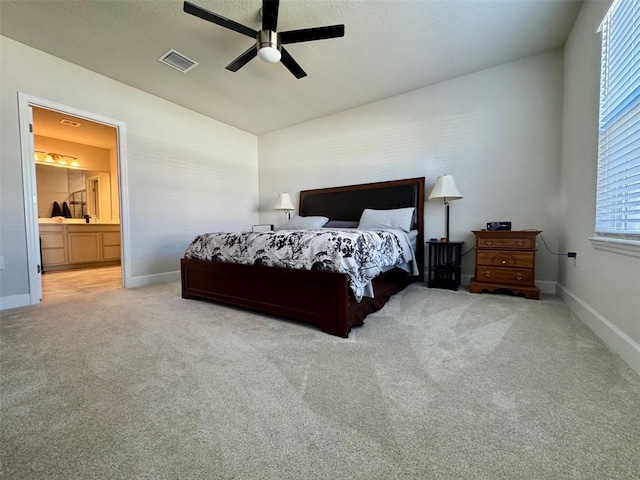 carpeted bedroom featuring ceiling fan, ensuite bathroom, and multiple windows