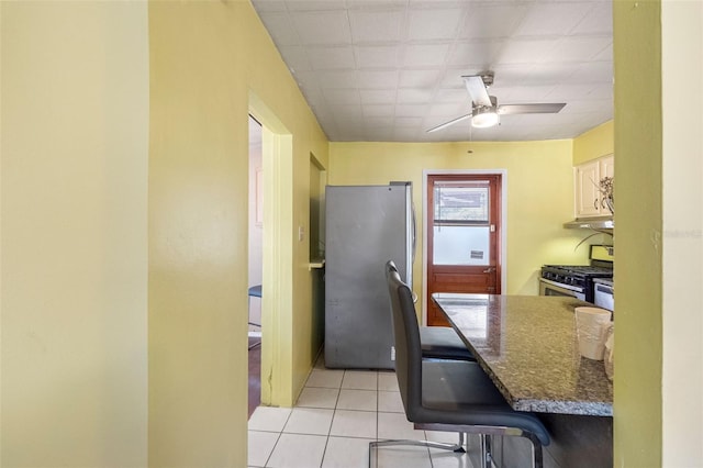 kitchen with stainless steel appliances, dark stone countertops, light tile patterned floors, and ceiling fan