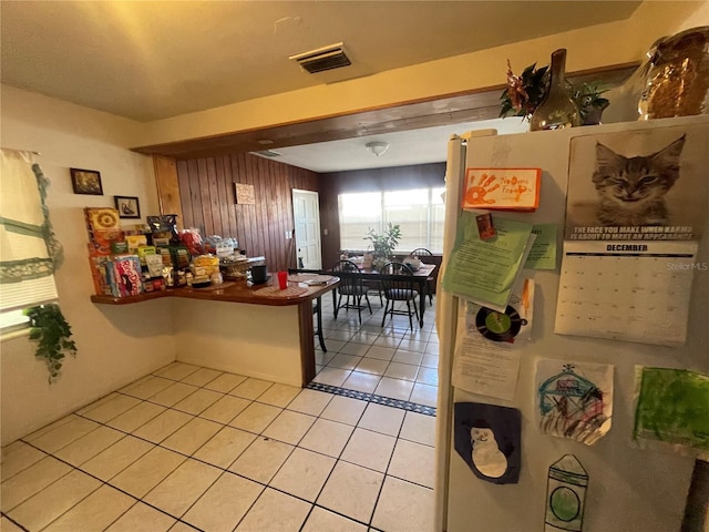 kitchen with wood walls, white fridge, and light tile patterned floors