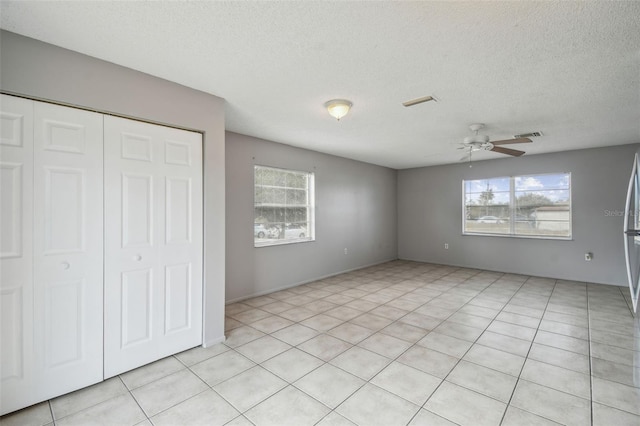 unfurnished bedroom with ceiling fan, a closet, light tile patterned flooring, and a textured ceiling