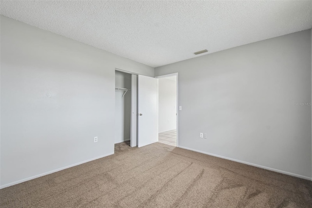 unfurnished bedroom featuring light colored carpet, a textured ceiling, and a closet