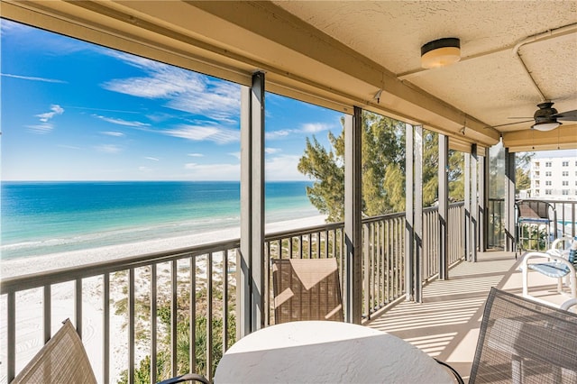 sunroom / solarium with ceiling fan, plenty of natural light, a water view, and a beach view