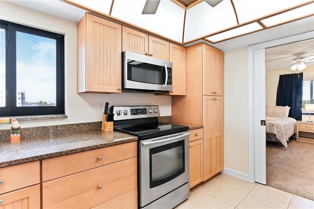 kitchen with light brown cabinetry, stainless steel appliances, light colored carpet, ceiling fan, and dark stone countertops