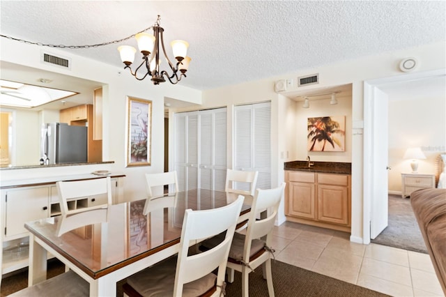 dining area with sink, light tile patterned flooring, a textured ceiling, and a notable chandelier