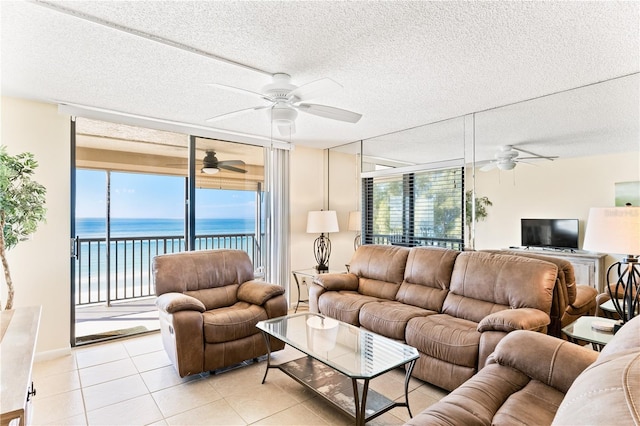 tiled living room featuring ceiling fan, a water view, and a textured ceiling