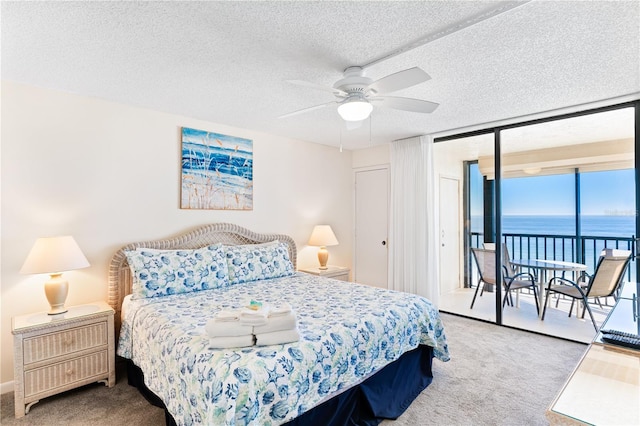 carpeted bedroom with access to exterior, ceiling fan, a water view, and a textured ceiling