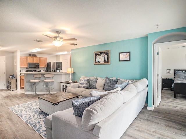 living room featuring a textured ceiling, light wood-type flooring, and ceiling fan