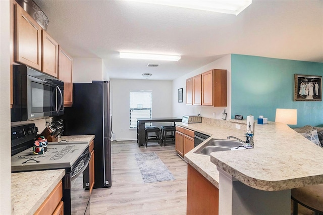 kitchen with sink, light hardwood / wood-style flooring, kitchen peninsula, a breakfast bar area, and black appliances