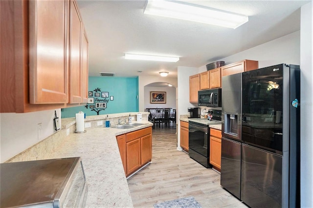 kitchen with kitchen peninsula, sink, black appliances, and light hardwood / wood-style flooring