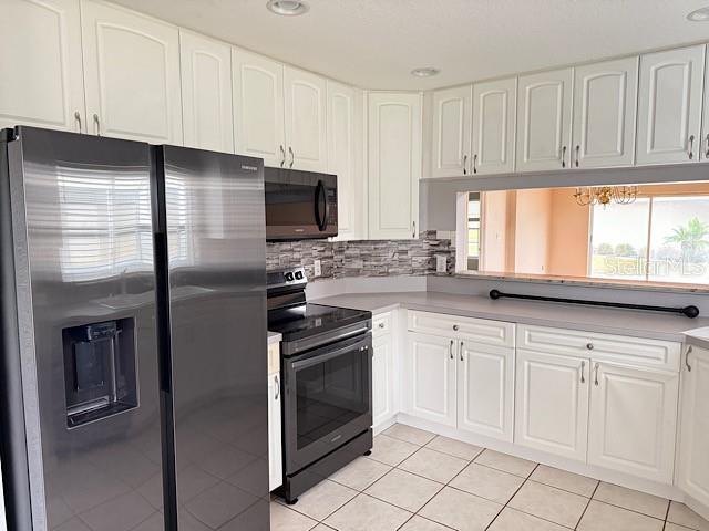 kitchen with black appliances, light tile patterned flooring, and white cabinets