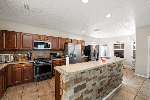 kitchen with backsplash, a kitchen island with sink, light tile patterned flooring, and appliances with stainless steel finishes