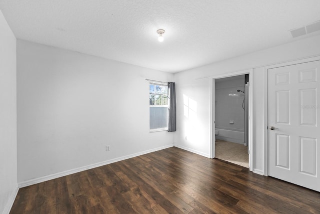 unfurnished bedroom with ensuite bathroom, dark hardwood / wood-style flooring, and a textured ceiling