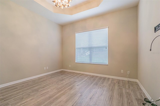 spare room with light wood-type flooring, an inviting chandelier, and a raised ceiling