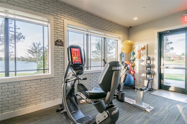 exercise room featuring a water view and brick wall