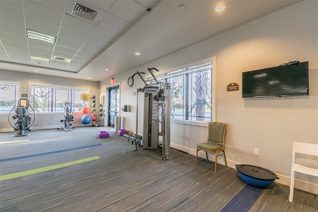 exercise room featuring carpet, a paneled ceiling, and brick wall