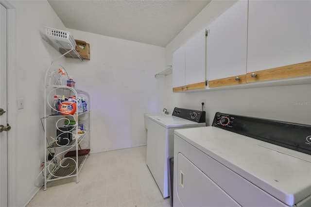 clothes washing area with washing machine and clothes dryer, cabinets, and a textured ceiling