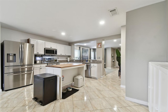 kitchen featuring stainless steel appliances, white cabinetry, wooden counters, and a center island