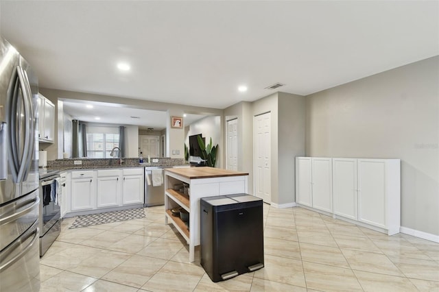 kitchen with wooden counters, kitchen peninsula, sink, white cabinetry, and stainless steel appliances