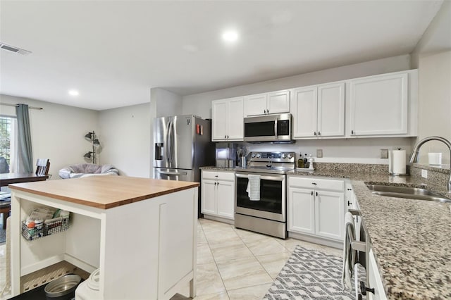 kitchen with a kitchen island, butcher block countertops, sink, white cabinetry, and stainless steel appliances