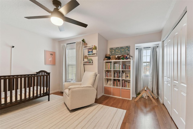 bedroom with ceiling fan, hardwood / wood-style floors, a closet, and a nursery area