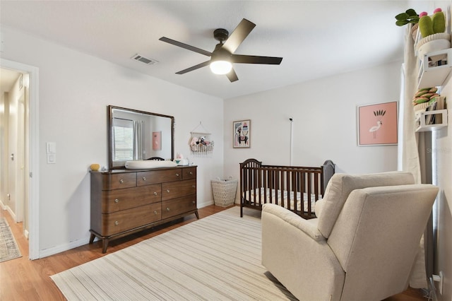 bedroom featuring ceiling fan, light hardwood / wood-style flooring, and a crib