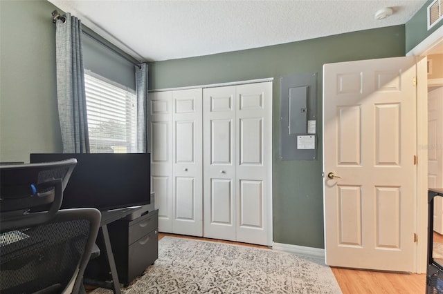 office featuring light wood-type flooring, electric panel, and a textured ceiling