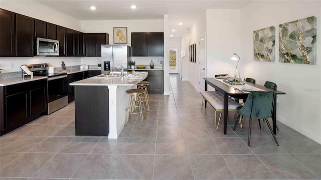 kitchen with a kitchen bar, stainless steel appliances, sink, light tile patterned floors, and a center island with sink