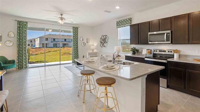 kitchen with a breakfast bar, sink, light tile patterned floors, an island with sink, and appliances with stainless steel finishes