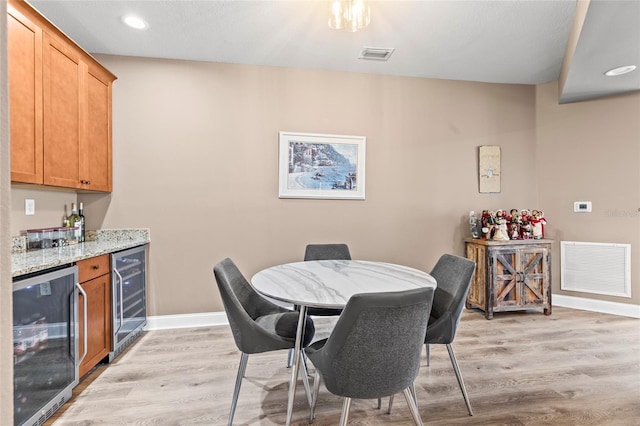 dining space with light wood-type flooring, indoor bar, and wine cooler