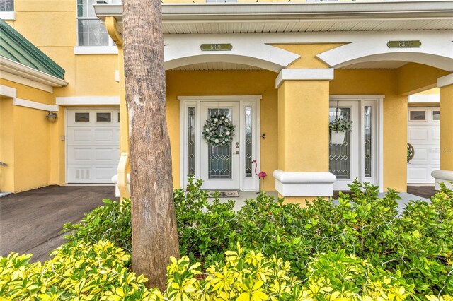 property entrance with a garage, aphalt driveway, and stucco siding