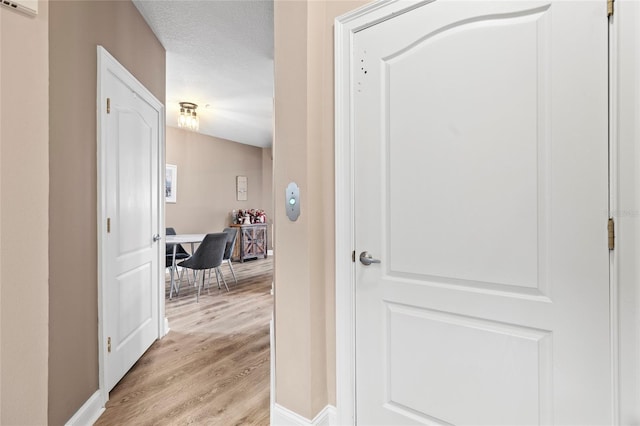 corridor featuring light wood-style floors, baseboards, and a textured ceiling