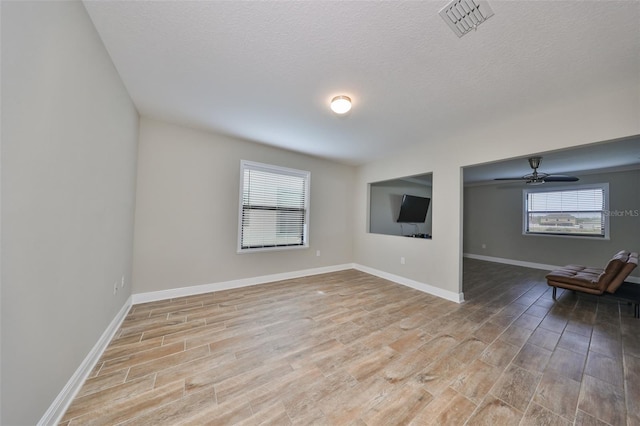 unfurnished room featuring ceiling fan, plenty of natural light, a textured ceiling, and light wood-type flooring